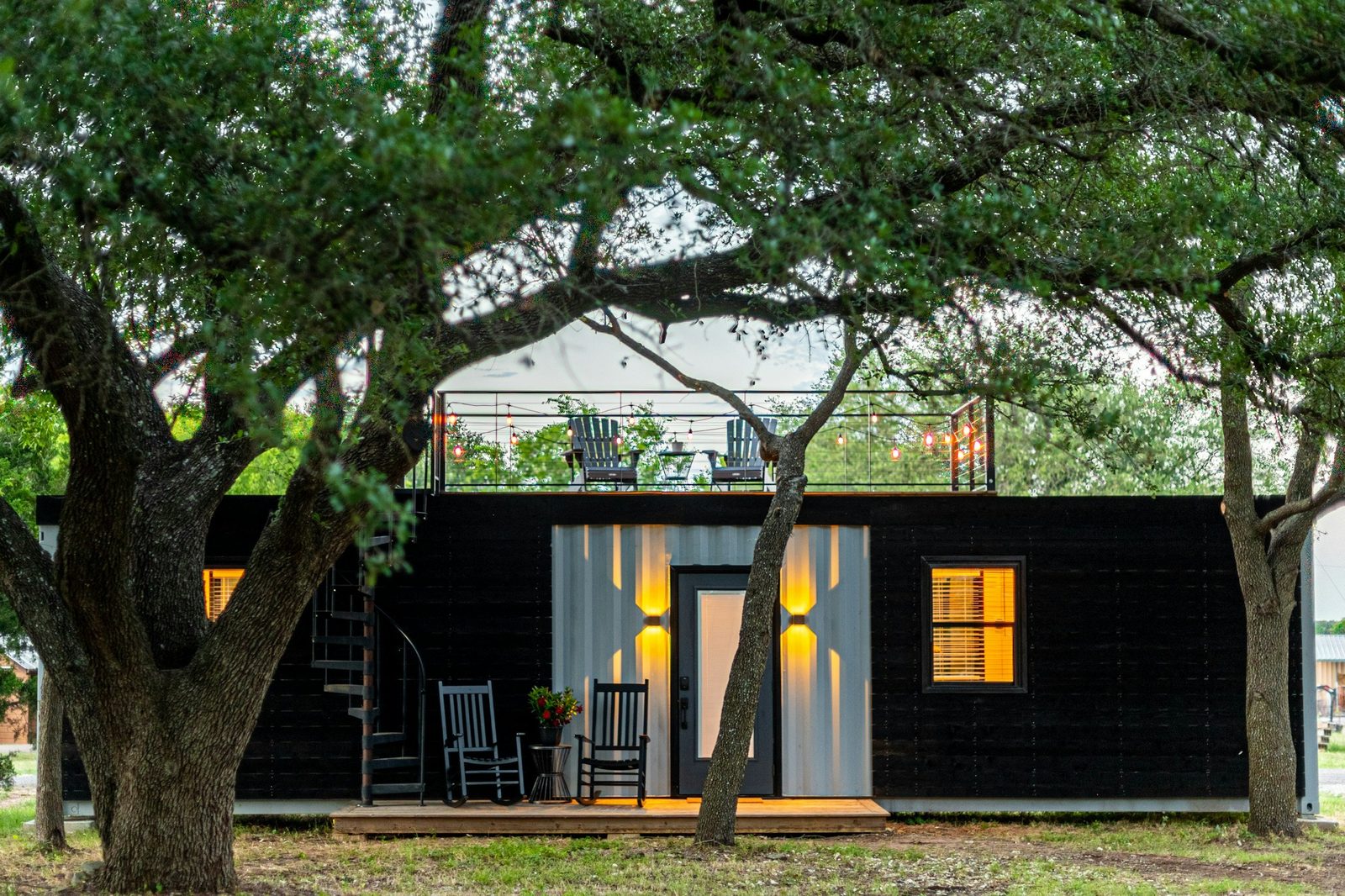 Black ADU with a lit entry and a rooftop deck under trees